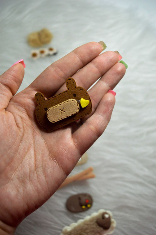 گیره مو کوچک طرح خرس قهوه ای نمدی با وصله بخیه دوزی شده و قلب زرد مینیاتوری